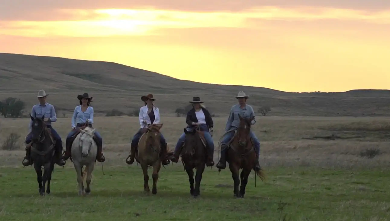 Five horseback riders in cowboy hats ride side by side across a grassy field at sunset, showcasing the ranching heritage and lifestyle at Drummond Ranch.