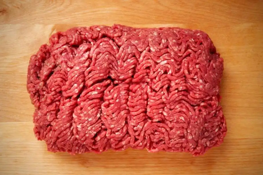 Fresh, uncooked ground beef with visible fat marbling on a wooden background, representing the high-quality grind from Drummond Ranch.
